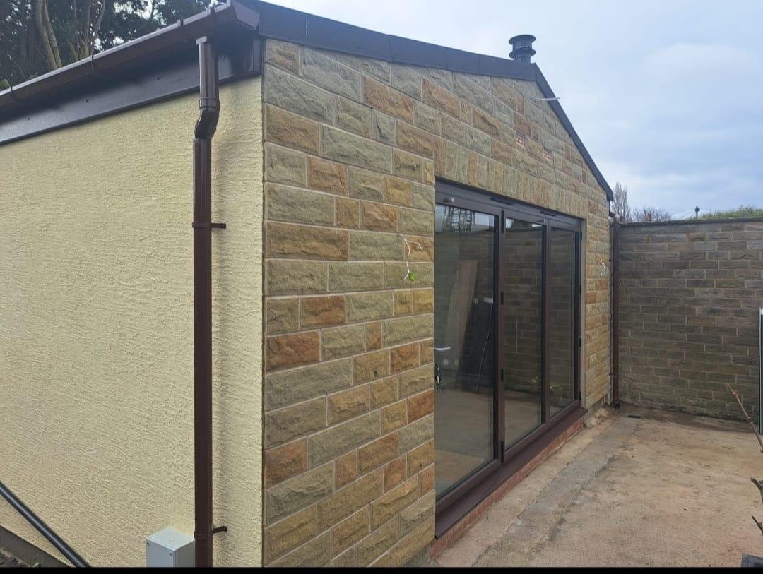 A completed single-storey rear extension with natural stone elevation, rendered gable and full-height bi-fold doors.