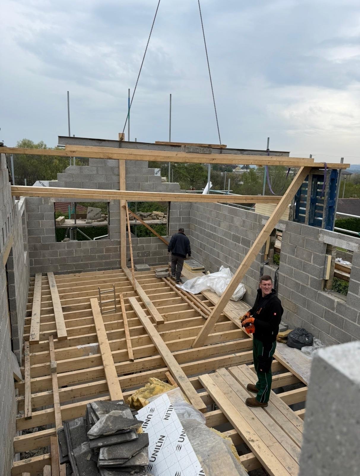 A two-storey new build under construction, with the first-floor joists and steel being craned into blockwork walls and two of the team on the deck.